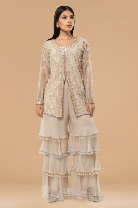 Beige jacket style embroidered tunic paired with multi layered gharara and crepe dupatta.